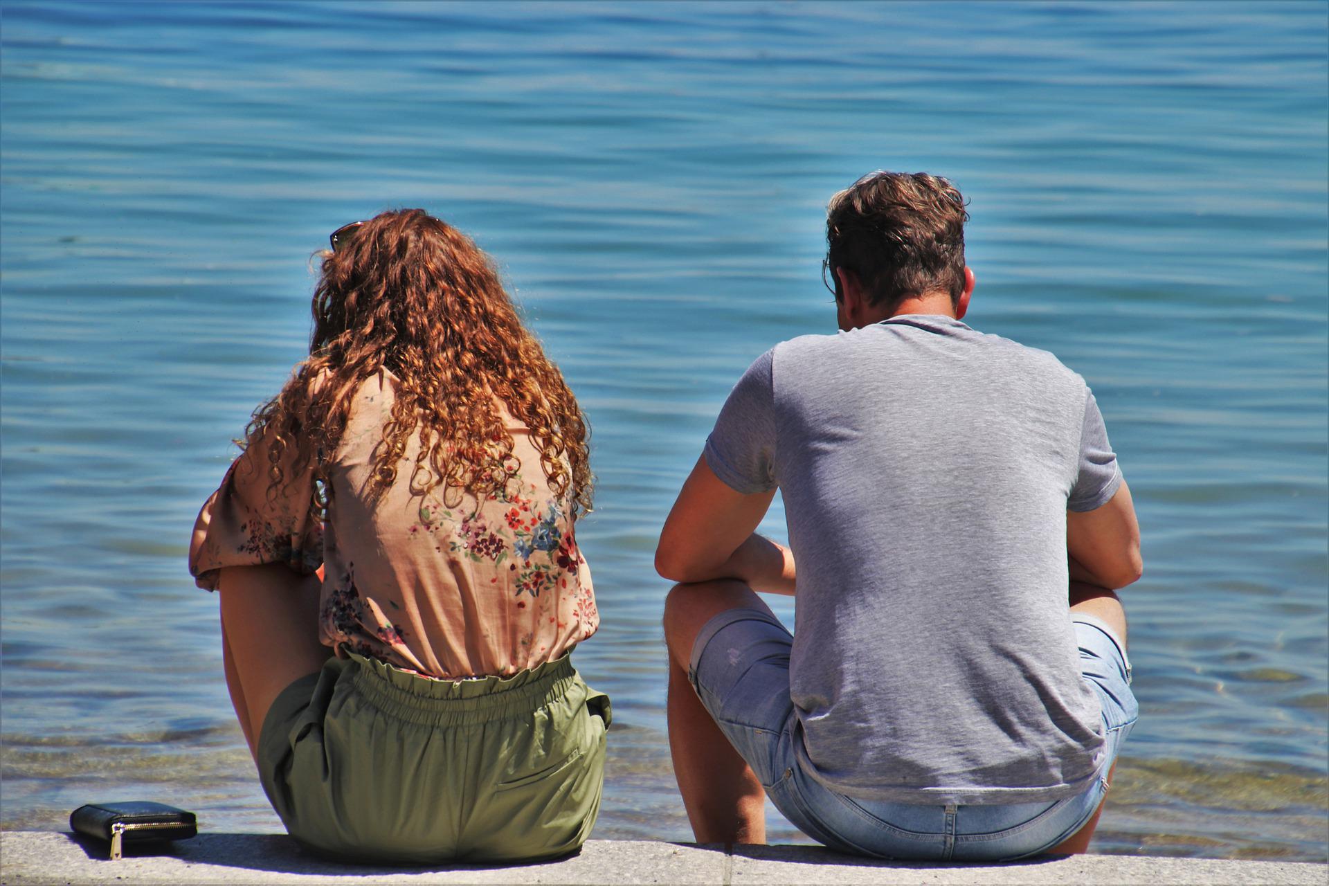 Couple sitting down next to each other on the beach seeming distant from one another or as if they had an argument.