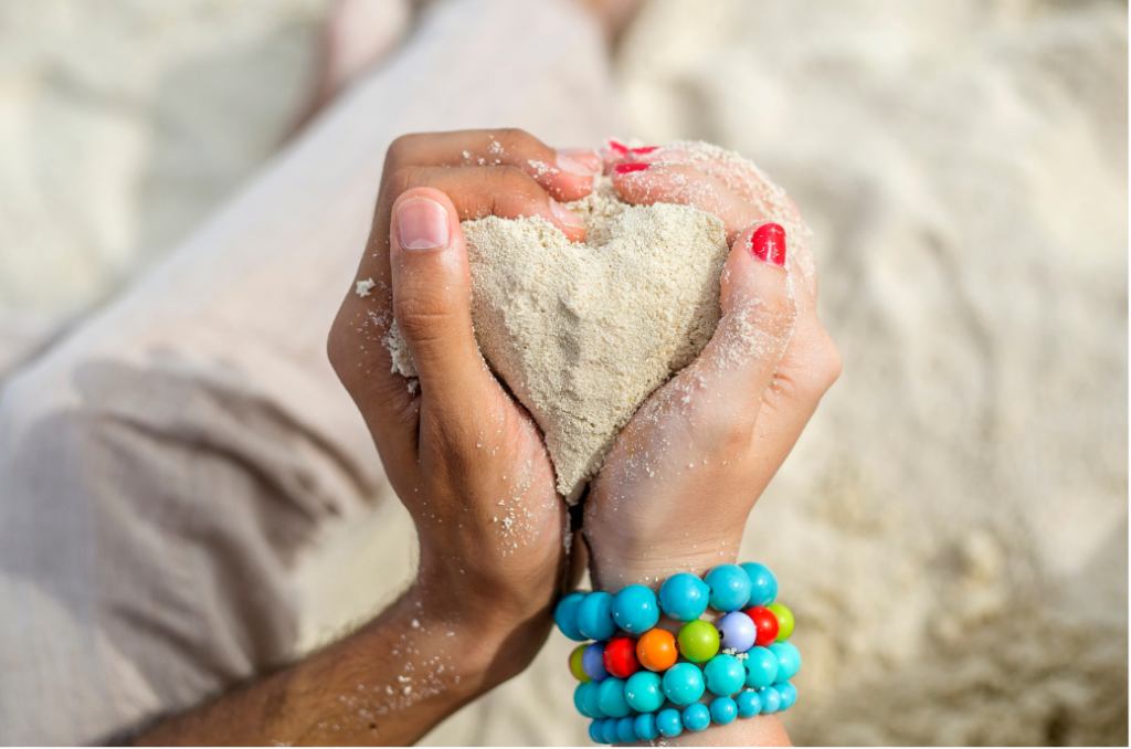 Couple uniting their hands together to form a heart made of sand.